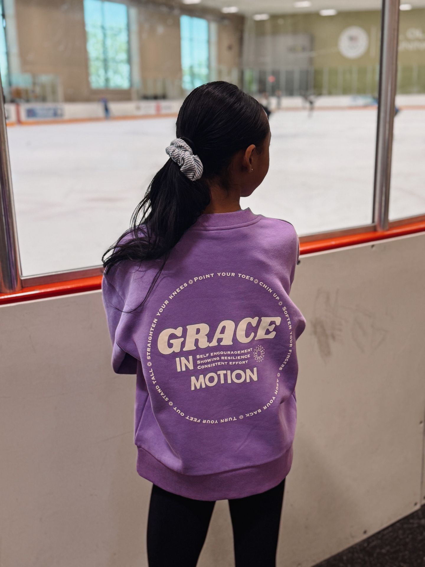 Skater wearing the orchid Grace in Motion crewneck from the back at the rink