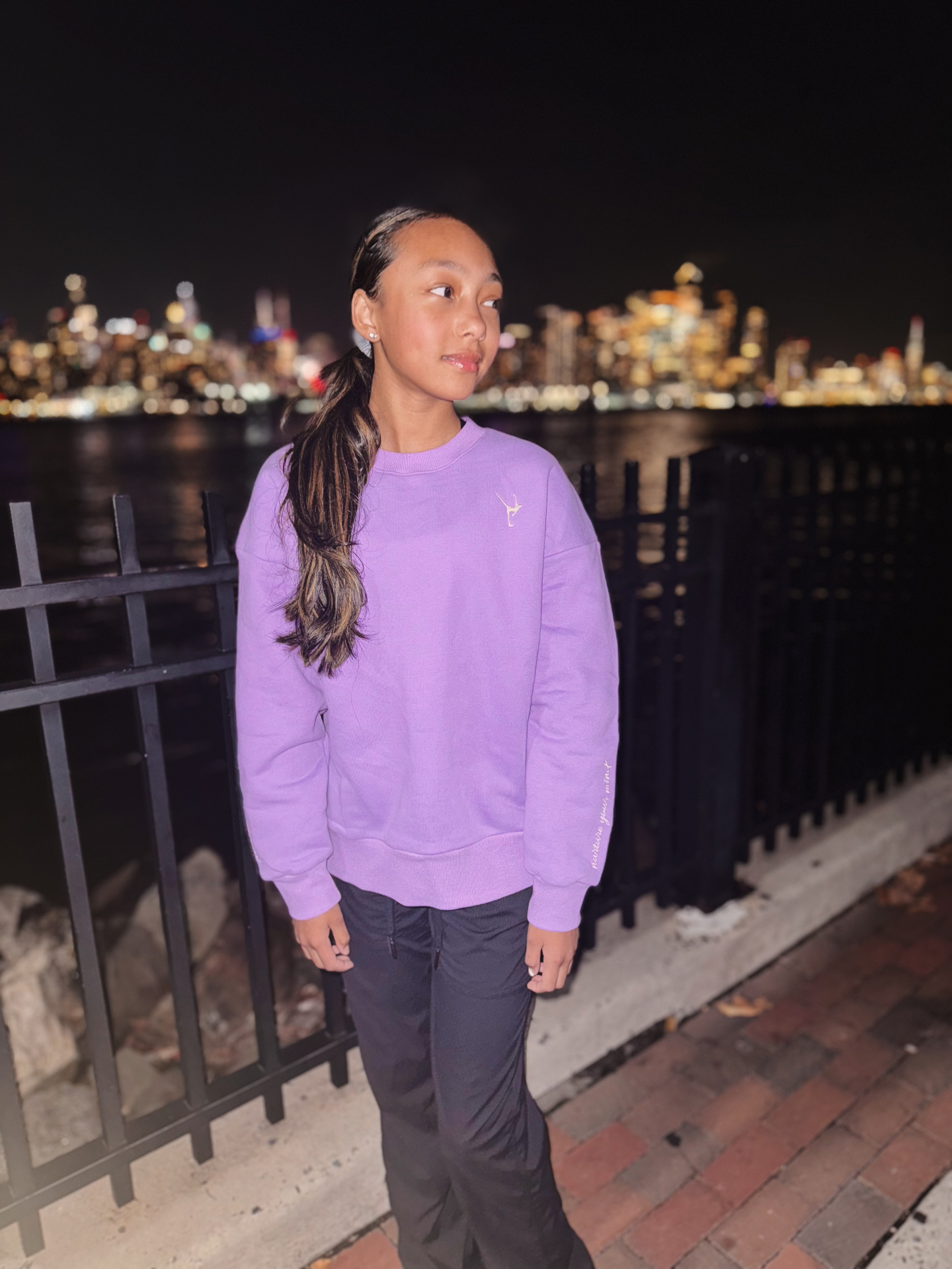 Skater wearing the orchid Grace in Motion crewneck at night by the waterfront