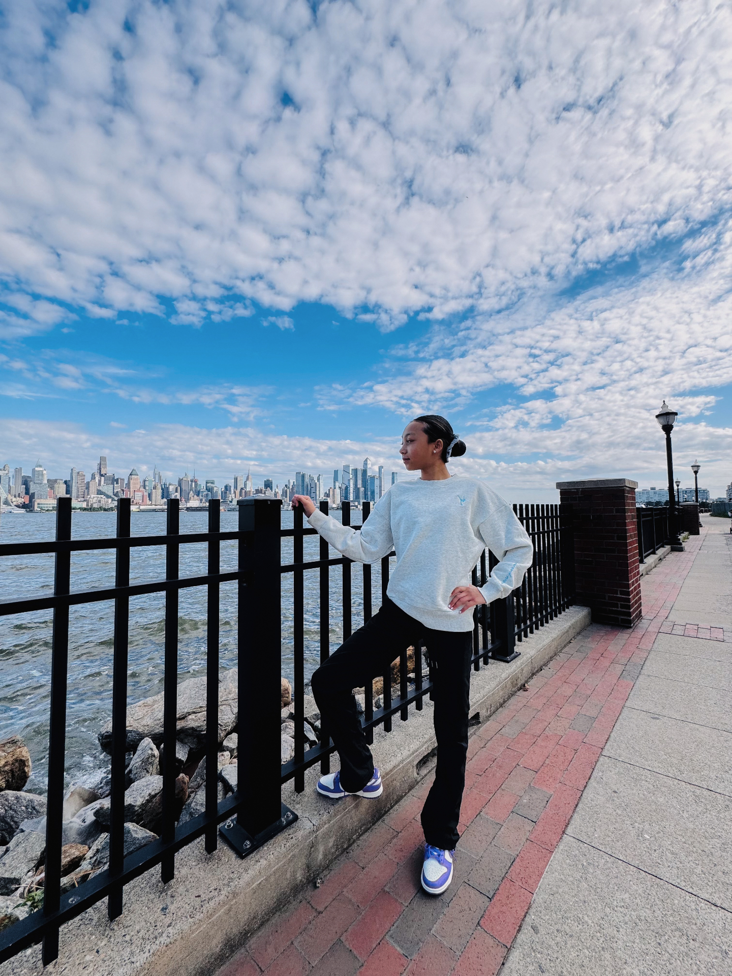 Customer wearing the mist Grace in Motion crewneck by the river with the city skyline