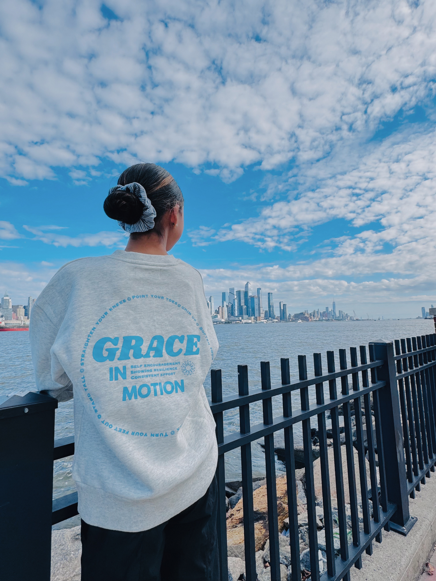Customer wearing the mist Grace in Motion crewneck showing the back print by the waterfront